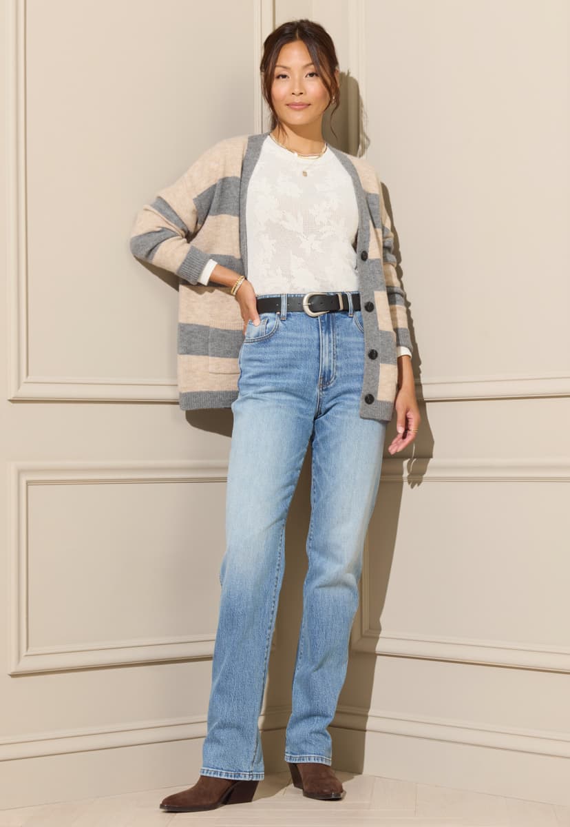 Woman wearing blue straight leg jeans with a white lace tee, striped cardigan, black belt, and brown boots. 