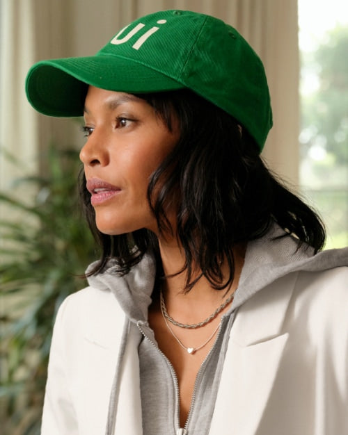 Image of a woman wearing a green baseball hat, grey hoodie, and white blazer.